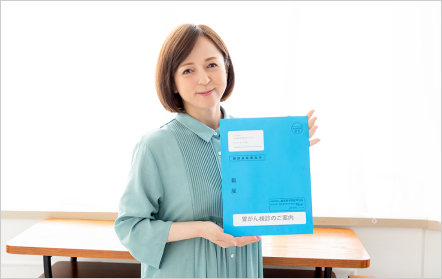 「がん検診のお知らせ」を持ついとうまい子さんの写真画像